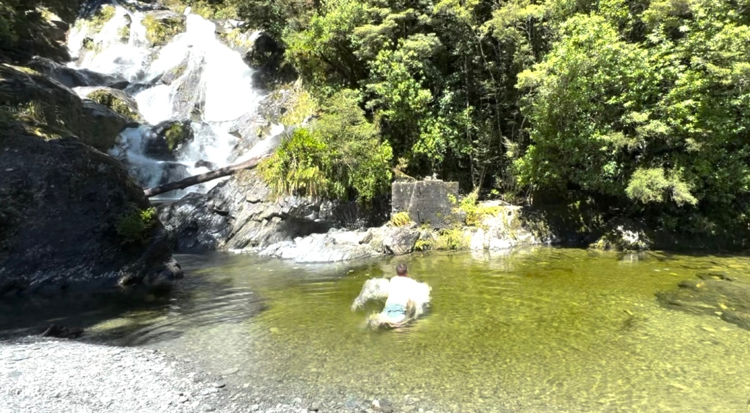 A man taking a cold dip at Fantail Falls off the Haast Pass in New Zealand